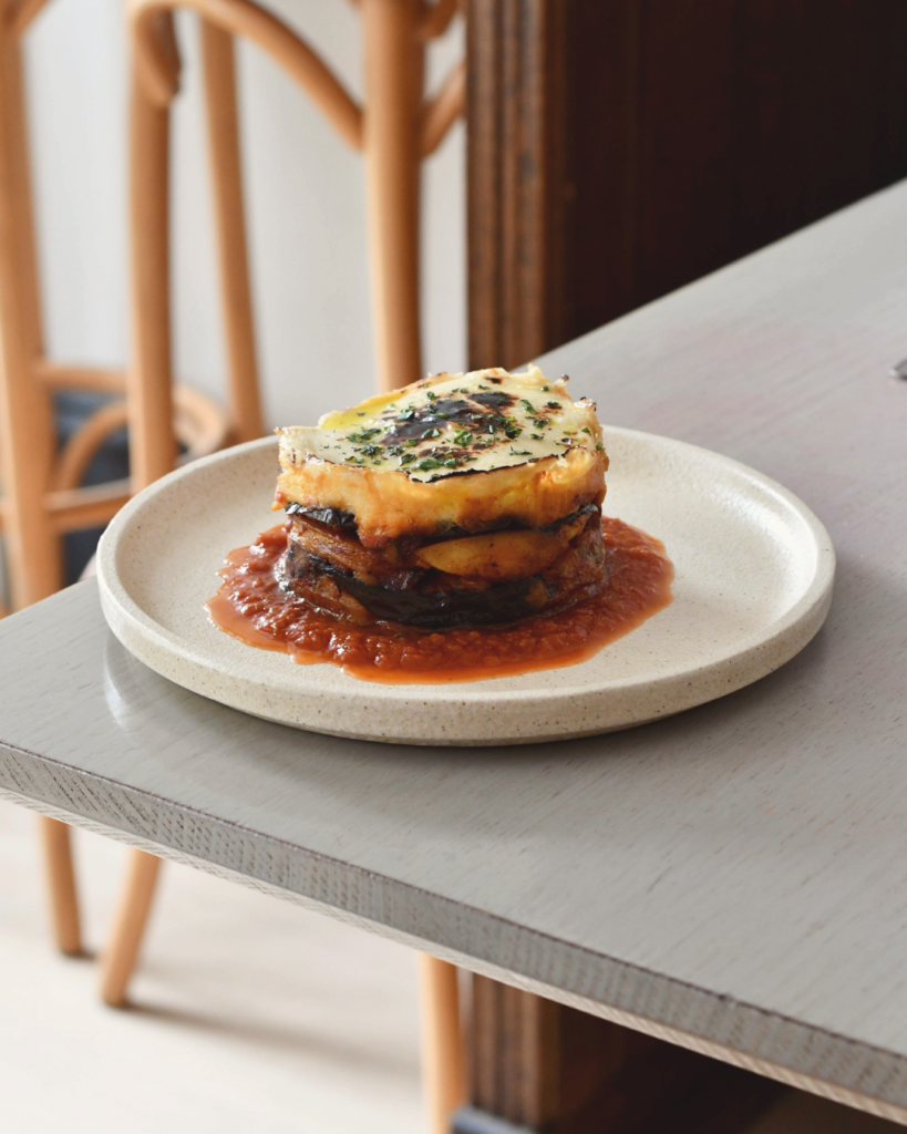 We create and curate beautiful clients for their PR and marketing needs. An appetising vegetarian moussaka sits on a well lit, pale grey table top.